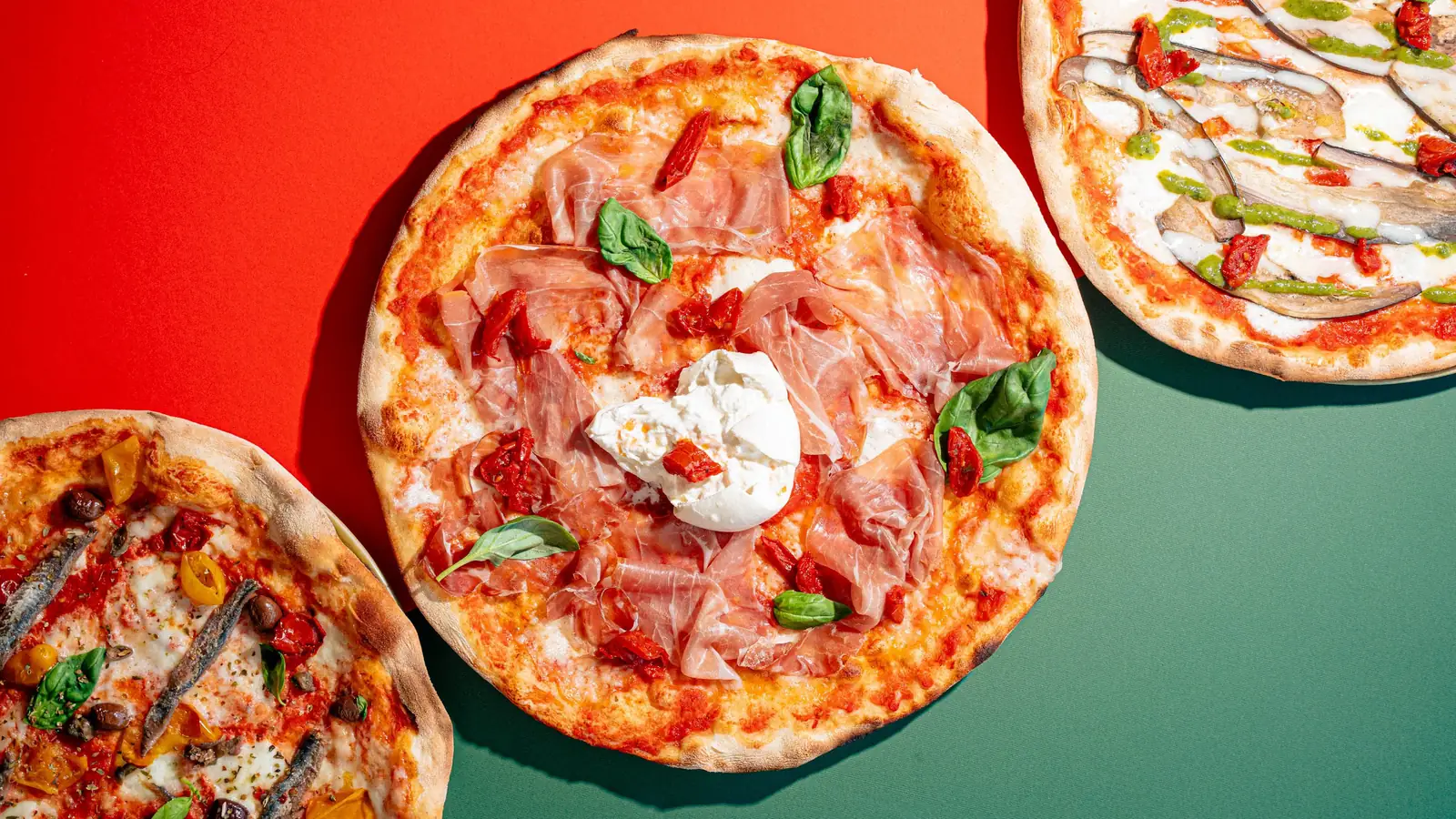 Pizze della Pizzeria Veneta viste dall'alto su fondo rosso e verde, con tovaglia a quadretti