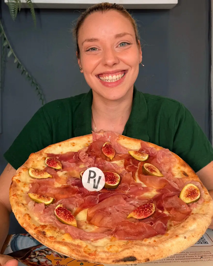 Rachele con la divisa della Pizzeria Veneta regge una pizza con crudo e fichi