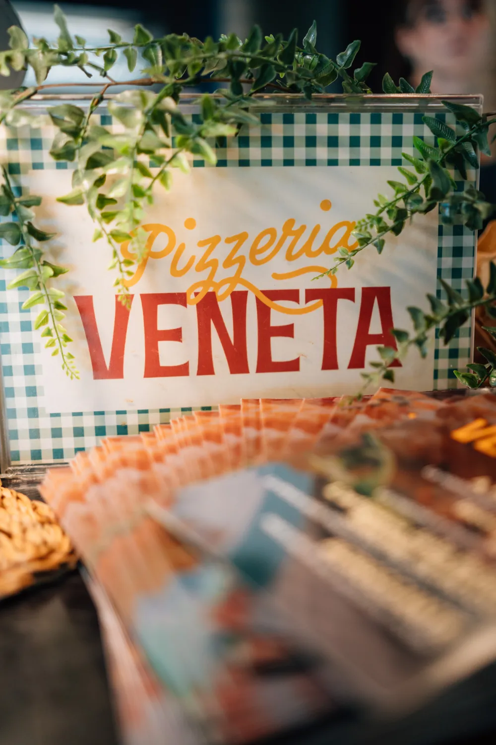 L'insegna Pizzeria Veneta su una tovaglietta a quadretti, tra le piante