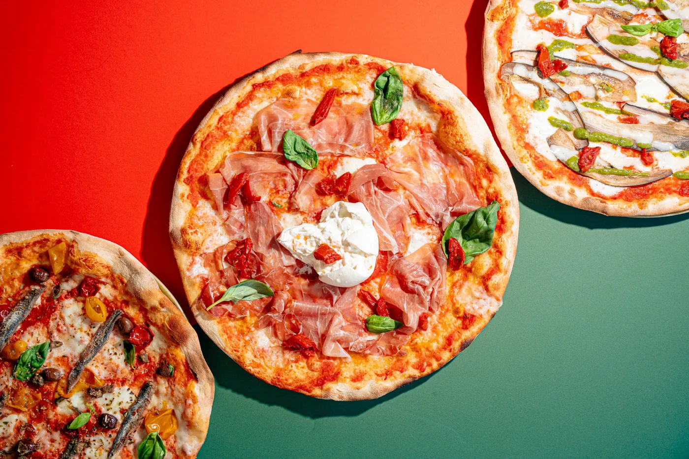 Pizze della Pizzeria Veneta viste dall'alto su fondo verde e rosso, con tovaglia a quadretti